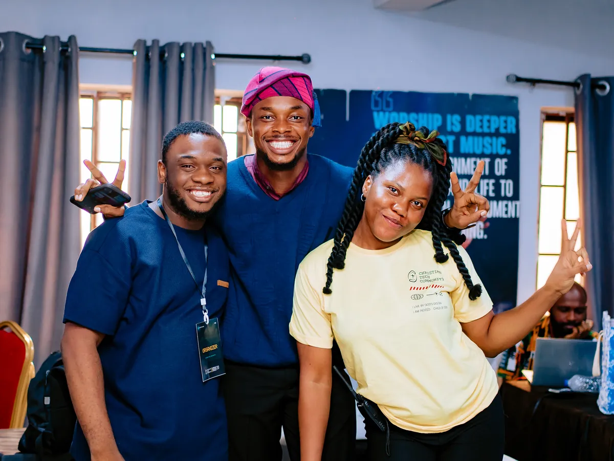 Three team members with lanyards smile and pose behind a desk at CTC 2.0.