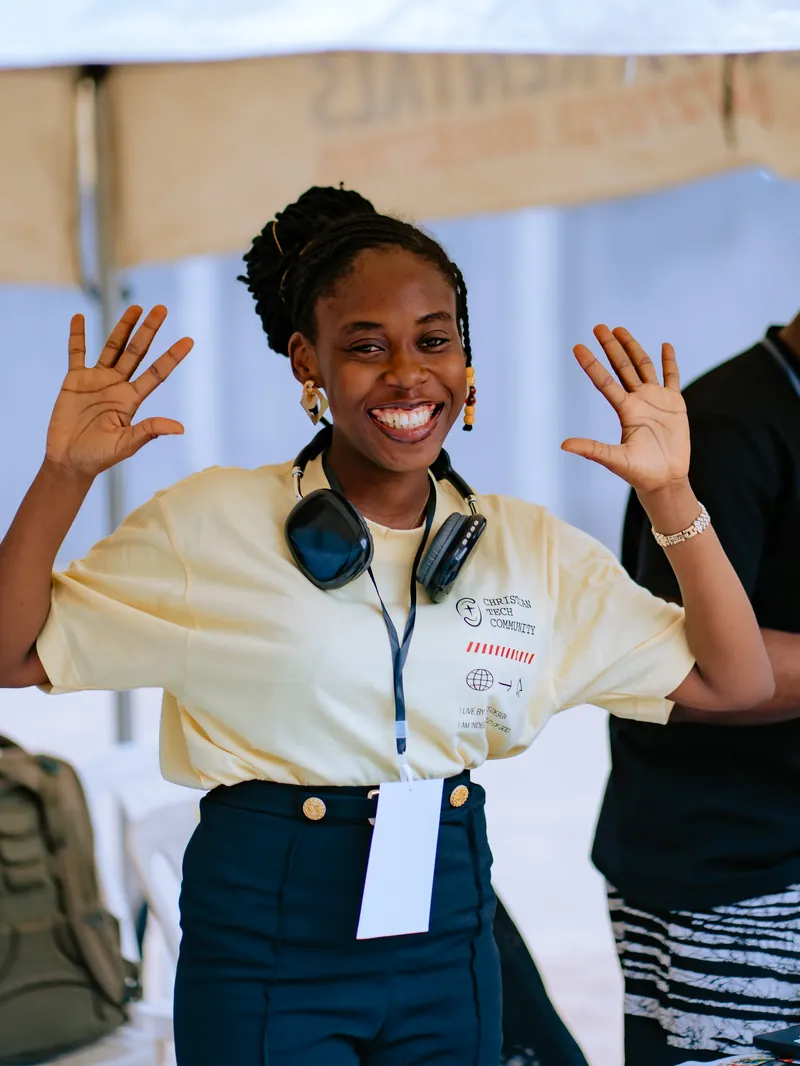 A smiling woman wearing a lanyard waves both hands at the camera at CTC 2.0.